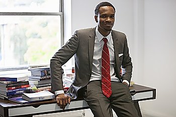 Portrait of happy African American businessman sitting on office desk