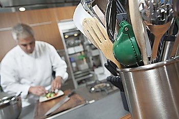 Mid- adult chef working with utensil holder in foreground