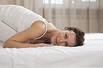 Mid adult woman kneels on bed smiling at camera