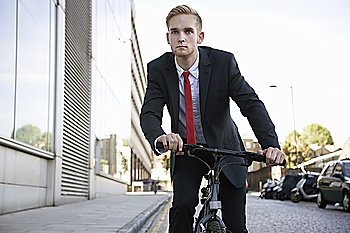 Handsome young businessman riding bicycle on street