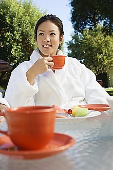 Young woman wearing bathrobe, drinking at outdoor table