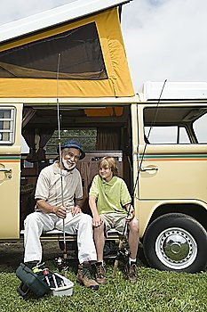 Grandfather and grandson sit with fishing rods in campervan