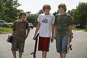 Three teenage brothers (13-17) walking on street carrying skateboards
