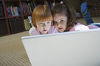 Young girls (5-6) lying on floor using laptop, contemplating