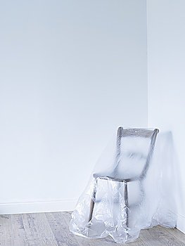 Chair covered by plastic in empty room corner