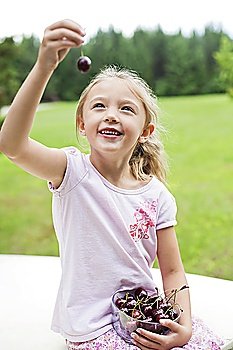 Happy young girl holding bowl full of bing cherries in park