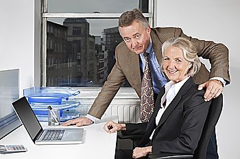Portrait of businesswoman and man with laptop at desk in office