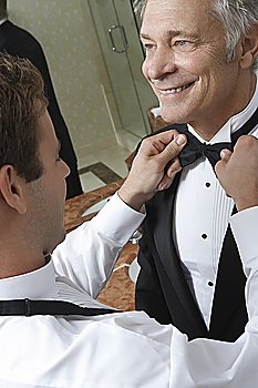 Young man tying middle-aged man´s bow tie