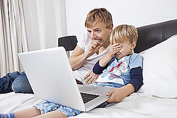 Father and son watching scary movie on laptop in bed