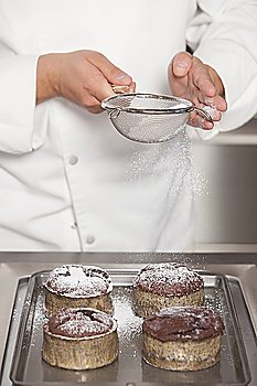 Mid- adult chef sieves icing sugar over chocolate cakes