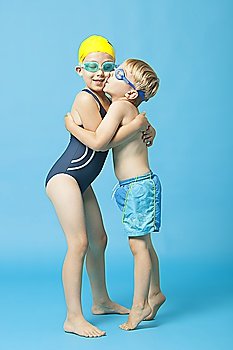 Young siblings in swimwear embracing and kissing over blue background