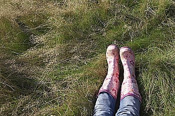 Person wearing pink galoshes lying in grass, low section