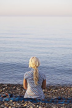 Young woman sitting on beach, back view