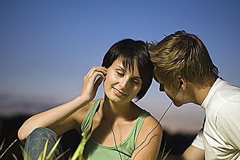 Couple sit listening to music on shared earphones