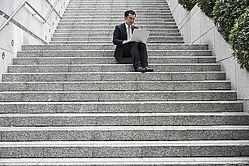 China, Hong Kong, business man sitting on steps using laptop, low angle view