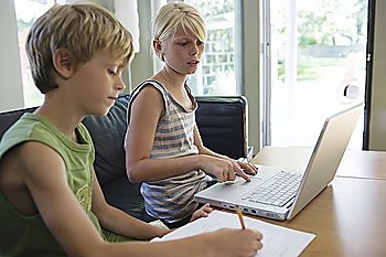 Siblings (6-8) sitting at table doing homework with laptop