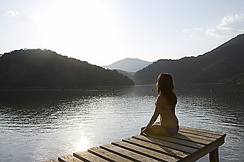 Young woman sits on lakeside jetty at dawn