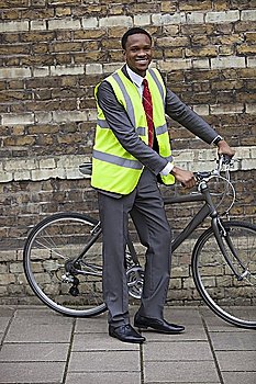 Happy young male engineer with bicycle against brick wall