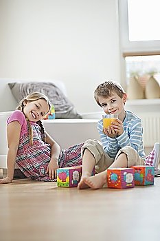 Portrait of young boy drinking orange juice while sitting with sister on floor