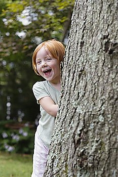 Portrait of girl (3-4) peeking from behind tree, laughing