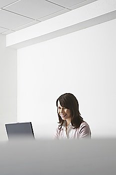 Woman sitting in office, using laptop and smiling