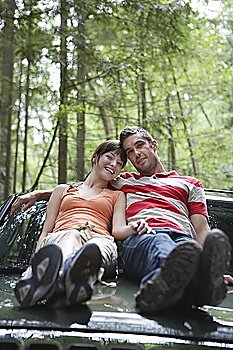 Couple sitting on car bonnet in forest, portrait