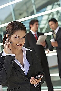 Businesswoman using earpiece with businessmen in background