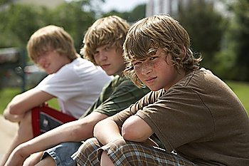 Three teenage brothers (13-17) sitting on street curb portrait