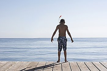 Boy (10-12) standing on jetty in snorkelling mask, back view