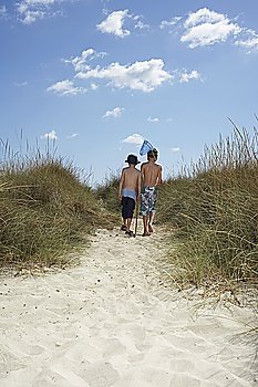 Two boys (6-11) walking in sand dunes with fishing net, back view