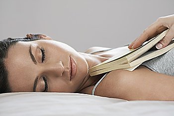 Young woman holding book asleep on bed, close-up