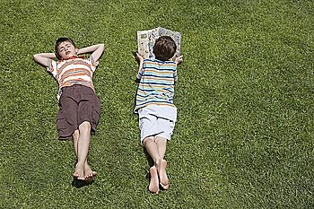 Two boys (6-11) lying on grass, one reading, elevated view