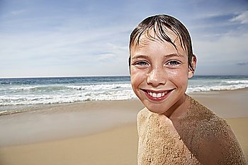 Boy (10-12) covered in sand, smiling on beach, portrait