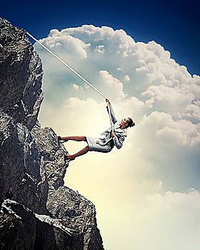 businesswoman climbing steep mountain hanging on rope