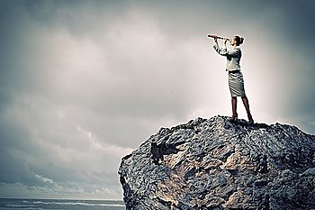 Image of businesswoman looking in telescope standing atop of rock