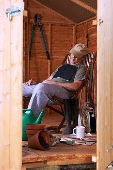 Man sitting in deckchair falling asleep in the shed while reading book