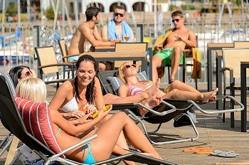 Chatting girls lying on deckchair sunbathing in bikinis sunny day