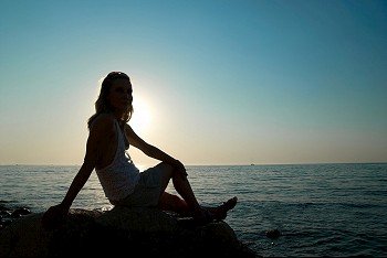 Young woman silhouette against blue sea and sunset