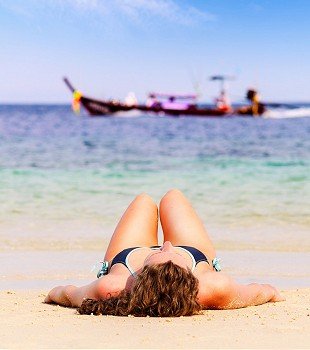young woman is lying on beach with long tail boat on background