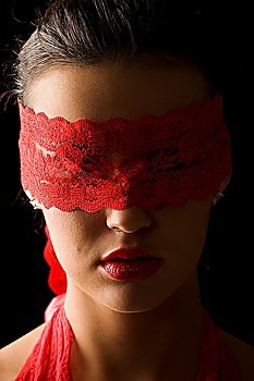 nice and mysterious portrait of a young brunette on black background with a red mask of lace