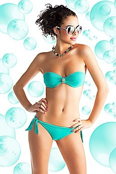 cute sexy brunette in green bikini with white sunglasses and curly hair style over white, she is in front of the camera with face turned of three quarters at left and has both hands on the hips