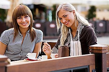 young cute elegant woman sitting outdoor in a cafe in a city with coffee and smiling