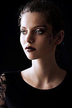 close up portrait of very beautiful young lady actrees over a dark background with dirty make up and fashion light, she is turned of three quarters at right and looks in front of her