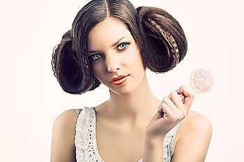 young beautiful brunette with a creative luxury hair style and a colored lollipop. She looks in to the lens and has the face slightly folded at right. She tales the lollipop with left hand.