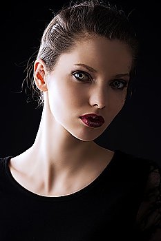 close up portrait of very beautiful young lady actrees over a dark background with dirty make up and fashion light, she is turned of three quarters at left and she looks in to the lens with intense expression