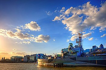 HMS Belfast docked on River Thames in London bathed in late afternoon sunlight