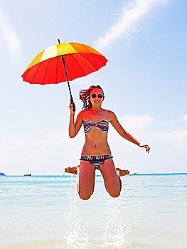 girl jumping on the beach with a red umbrella