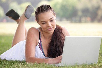 attractive young student working on lap top while lying on grass in park