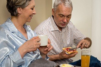 Elderly couple eating romantic breakfast together in bed
