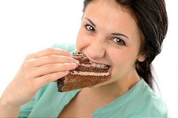 Greedy young woman eating tasty cake looking at camera